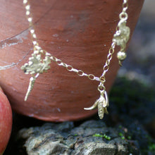 Gold bracelet with a small pendant on an antique clay plant pot against a natural background.