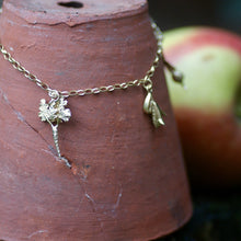 Gold necklace with a pendant on a terracotta pot with an apple in the background
