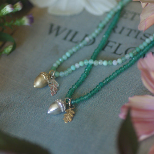Two green beaded necklaces with leaf pendants on a book titled 'Wild Flowers'.