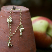 Gold bracelet with vegetable charms on a terracotta pot with apples in the background