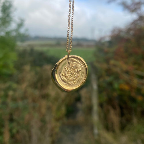 Gold necklace with a round pendant held by a hand against a blurred natural background