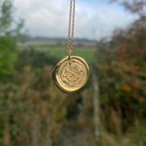 Gold necklace with a round pendant held by a hand against a blurred natural background