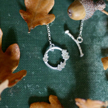 Silver necklace with a wreath pendant on a green fabric background with leaves.